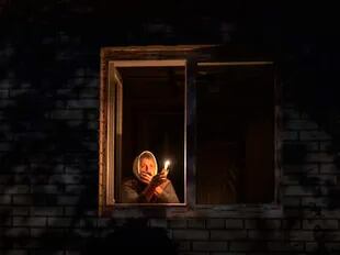 Una mujer alumbra con una vela desde su ventana ante los cortes de electricidad en Ucrania