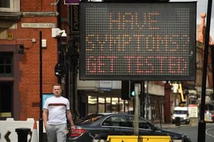 Los peatones pasan en frente de un tablero electrónico que insta someterse a un test si tienen síntomas de Covid-19 en Bolton, noroeste de Inglaterra, el 9 de septiembre de 2020