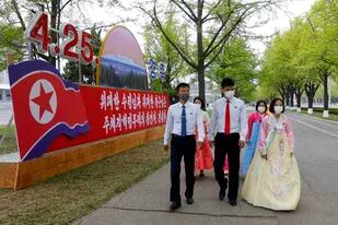 Varias personas con vestimenta formal pasan junto a un afiche que conmemora el 90mo aniversario de la fundación del Ejército Revolucionario del Pueblo Coreano el lunes 25 de abril de 2022, en Pyongyang, Corea del Norte. El afiche dice: "Raiz histórica de nuestra revolución". (AP Foto/Jon Chol Jin)