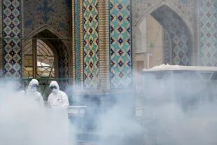 Miembros de un equipo médico rocían desinfectante para desinfectar una mezquita en Mashhad