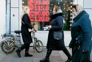 FILE - People walk past a screen in a currency exchange office showing the exchange rates of the US dollar and the euro against the ruble in Moscow on February 28, 2022. (AP Photo / Pavel Golovkin, File)