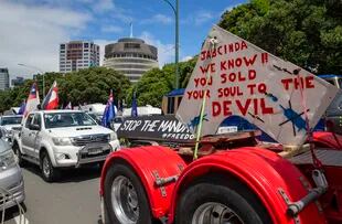 Una caravana de vehículos bloquea una avenida cerca del Parlamento el martes 8 de febrero de 2022, en Wellington, Nueva Zelanda. El letrero menciona a la primera ministra Jacinda Arden y dice: "sabemos que le vendiste tu alma al diablo". 