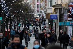 Los peatones, algunos con mascarilla o cubriéndose la cara debido a la pandemia de coronavirus, pasan frente a las tiendas cerradas en Oxford Street en el centro de Londres el 20 de diciembre de 2020