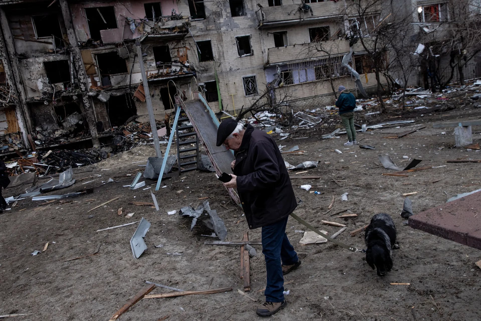 Un hombre pasea a su perro frente a un bloque residencial destruido que fue alcanzado por un ataque con misiles a primera hora de la mañana, el 25 de febrero de 2022 en Kiev, Ucrania.