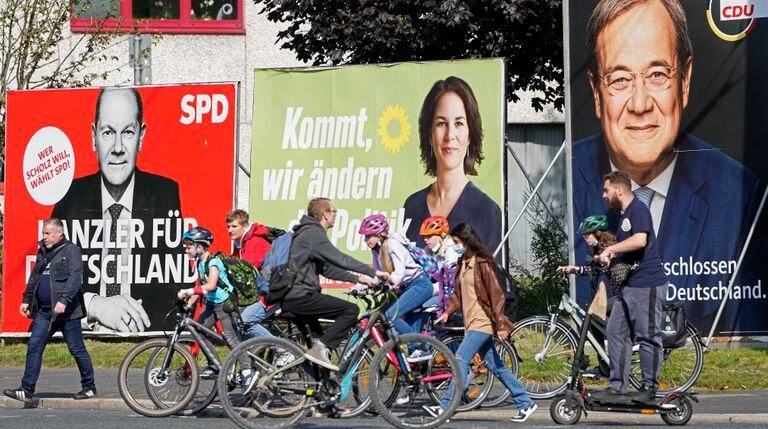 ARCHIVO - En esta imagen del jueves 23 de septiembre de 2021, gente pasando ante  carteles electorales de los tres candidatos a canciller de Alemania: Desde la derecha: Armin Laschet, de la Unión Democristiana (CDU), Annalena Baerbock, del Partido Verde alemán (Die Gruenen), y Olaf Scholz, del Partido Socialdemócrata (SPD), en una calle de Gelsenkirchen, Alemania. (AP Foto/Martin Meissner, Archivo)
