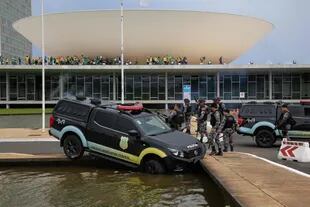 Miembros de la Policía Federal Legislativa junto a un vehículo que se estrelló contra una fuente cuando los partidarios del expresidente brasileño Jair Bolsonaro invaden el Congreso Nacional