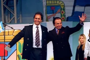 (1997) Daniel Scioli y Carlos Menem, envueltos en el decorado peronista para la campaña. De fondo, Karina Rabolini