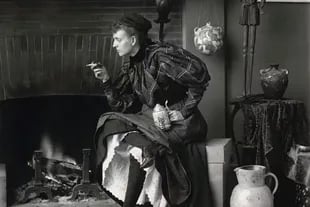 Autorretrato de Frances Benjamin Johnston como ‘nueva mujer’, sentada frente a la chimenea, mirando hacia la izquierda, con un cigarrillo en una mano y una jarra de cerveza en la otra, en su estudio de Washington, D.C.