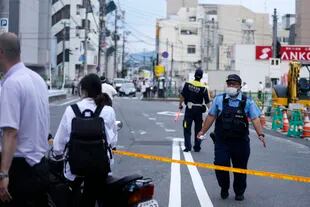 Police direct pedestrians and vehicles near the spot where former Prime Minister Shinzo Abe was shot while delivering a speech in Nara, Japan, Friday, July 8, 2022. Abe's murder has caused shock in a country whose control laws of weapons are among the strictest in the world.  (Kyodo News via AP)