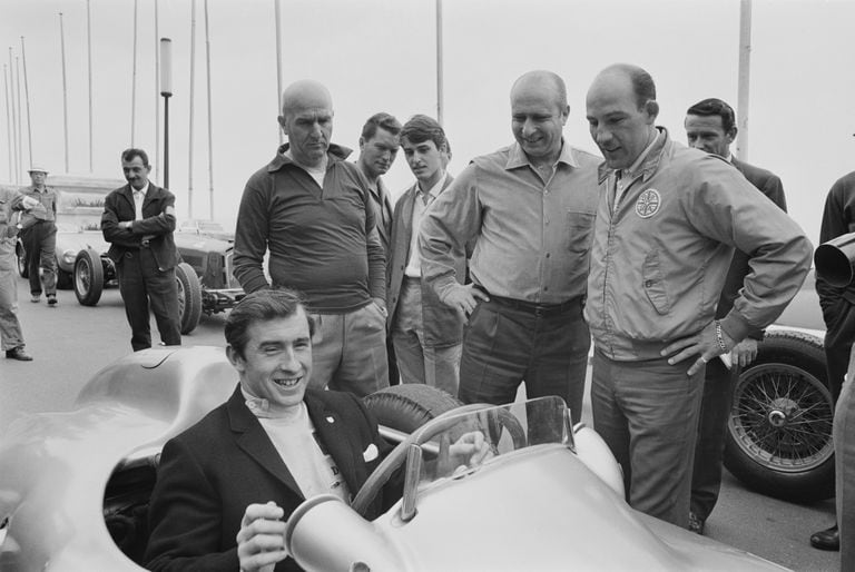 Jackie Stewart a bordo de un coche de carreras sonríe con el piloto británico de Fórmula Uno Sirling Moss, el piloto argentino Juan Manuel Fangio y el piloto italiano Giuseppe Farina durante un evento después de la Gran Premio de Mónaco, 30 de mayo de 1965