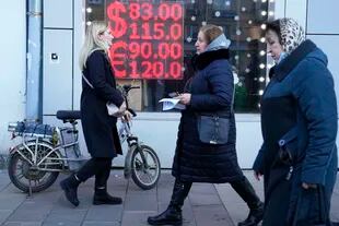 Tres mujeres pasan frente al tablero electrónico de una casa de cambios que muestra la cotización del dólar y el euro en Moscú el 28 de febrero del 2022. El rublo ruso se devaluó meses atrás como consecuencia de las sanciones económicas asociadas con la invasión rusa de Ucrania. (AP Photo/Pavel Golovkin, File)