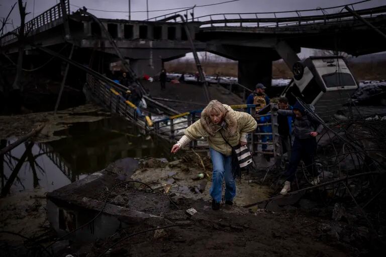 Una mujer huye con su familia a través de un puente destrozado a las afueras de Kiev, Ucrania, el 2 de marzo de 2023. (Foto AP / Emilio Morenatti)