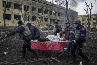 Empleados y voluntarios de emergencias ucranianos llevan a una mujer embarazada herida desde un hospital de maternidad dañado por los bombardeos en Mariupol, Ucrania, el 9 de marzo de 2022.