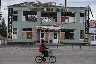 Una mujer pasa con su bici frente a un edificio destruido en la ciudad de Balaklia, en la región de Kharkiv, recapturada por los ucranianos