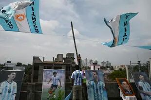 A member of an Argentina's national football team fan club stands amid pictures of Argentina's captain Leo Messi (center R) and the late Argentine football legend Diego Maradona (center L) in a rooftop ahead of the Copa America final match between Argentina and Brazil, in Kolkata on July 10, 2021. (Photo by Dibyangshu SARKAR / AFP)