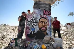 En Siria, tres hombres posan junto a un mural en solidaridad a George Floyd y las protestas en Estados Unidos contra el racismo y la brutalidad policial