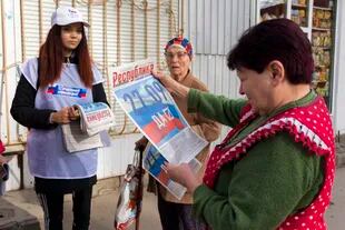 Una voluntaria de la comisión electoral regional distribuye periódicos a los ciudadanos locales antes de un referéndum en la República Popular de Lugansk controlada por los separatistas respaldados por Rusia, en el este de Ucrania, el jueves 22 de septiembre de 2022. 