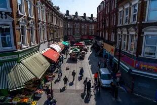 Los peatones caminan por los puestos del mercado en Electric Avenue en Brixton, sur de Londres el 23 de abril de 2020, mientras la vida en Gran Bretaña continúa bajo confinamiento para detener la propagación del coronavirus