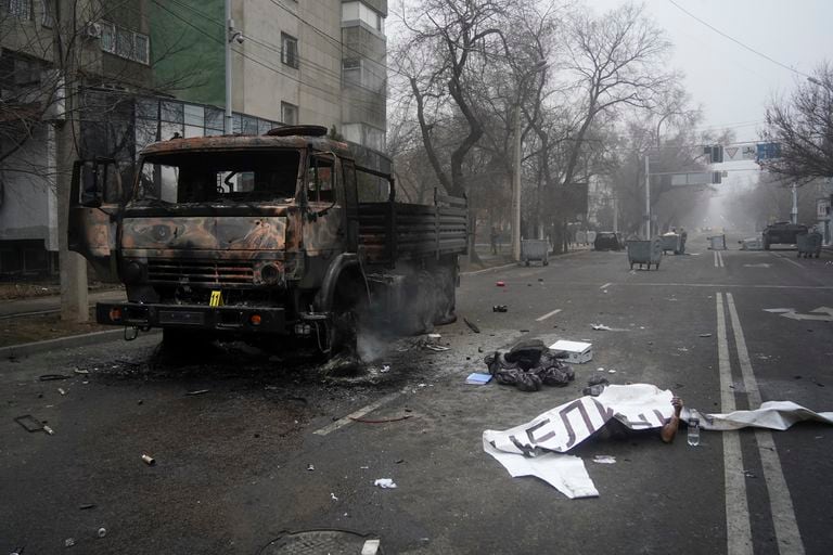 El cadáver de un fallecido, cubierto con una pancarta (derecha), junto a un camión militar calcinado durante los disturbios en Almaty, Kazajistán, el 6 de enero de 2022. (AP Foto/Vladimir Tretyakov/NUR.KZ via AP)