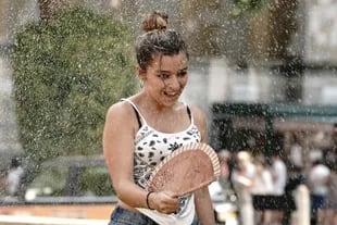 Una giovane donna sta con un ventilatore sotto la testa di un irrigatore davanti al Queen Elizabeth II Center.  Secondo il servizio meteorologico Met Office, le temperature potrebbero aumentare fino a 41 gradi in alcune parti dell'Inghilterra.