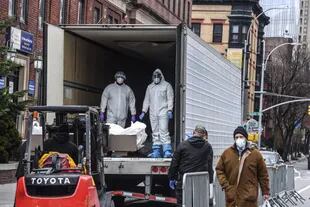 Los trabajadores médicos llevan un cuerpo a un camión refrigerado frente al Hospital de Brooklyn