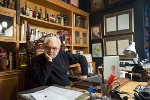 Pacho O'Donnell, en su escritorio, junto a una biblioteca que, entre otros tesoros, reúne 4 premios Martín Fierro