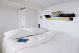 Este dormitorio, como el resto del espacio, fue revestido con madera pintada de blanco para una sensación de pulcritud general y también de desahogo a pesar de lo bajo del cielo raso.