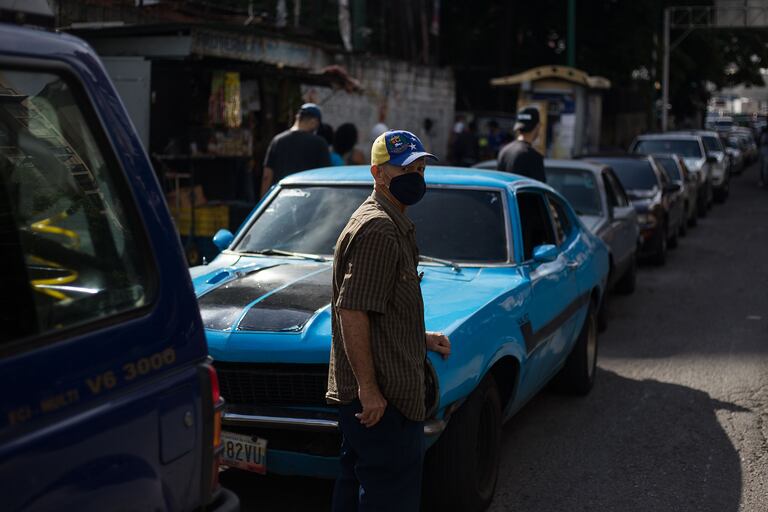 Un hombre espera junto a su auto en una fila para cargar el tanque de su vehículo cerca de una gasolinera en Caracas el 5 de octubre de 2020