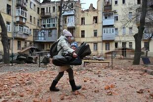 Una residente local lleva a su bebé fuera de su edificio residencial parcialmente destruido después de un ataque con misiles en Kharkiv el 30 de enero de 2023, en medio de la invasión rusa de Ucrania