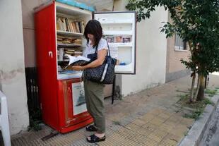 Una vecina del pasaje Praga, en Parque Chas, revisa los libros de la Biblioteca Libre de Praga, instalada en una vieja heladera 