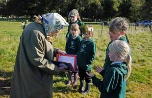Los niños de la escuela primaria Crathie presentan a la reina Isabel II de Gran Bretaña una tarjeta, después de que la reina y el príncipe Carlos, Príncipe de Gales, plantaran un árbol para marcar el inicio de la temporada oficial de siembra del Queen's Green Canopy en el Balmoral Cricket Pavilion, Escocia, el 1 de octubre de 2021