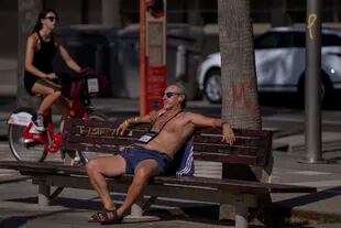 A man sunbathes sitting in a bench in Barcelona, Spain, Thursday, June 16, 2022. Spain's weather service says a mass of hot air from north Africa is triggering the country's first major heat wave of the year with temperatures expected to rise to 43 degrees Celsius (109.4 degrees Fahrenheit) in certain areas. (AP Photo/Emilio Morenatti)