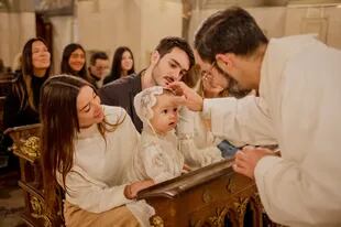 En brazos de su madrina, recibe la bendición del sacerdote de la parroquia San Nicolás de Bari.