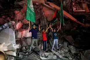 Niños palestinos ondean la bandera verde de Hamas y la palestina sobre los escombros de un edificio derribado mientras celebran el acuerdo de alto el fuego entre Israel y el grupo insurgente