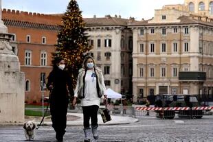 Mujeres con tapabocas caminan en la vacía Plaza Venecia de Roma