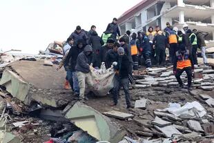 Un cuerpo es llevado en sábanas después de ser recuperado de debajo de los escombros de un edificio derrumbado en Kahramanmaras, cerca del epicentro del terremoto, el día después de que un terremoto de magnitud 7,8 azotara el sureste del país, el 7 de febrero de 2023. (Foto por Adem ALTAN / AFP)