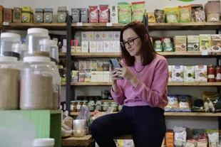 Lucila Nava en el local de productos naturistas, conectada a IG desde su celular porque es community manager y hace ambas tareas en paralelo durante todo el día
