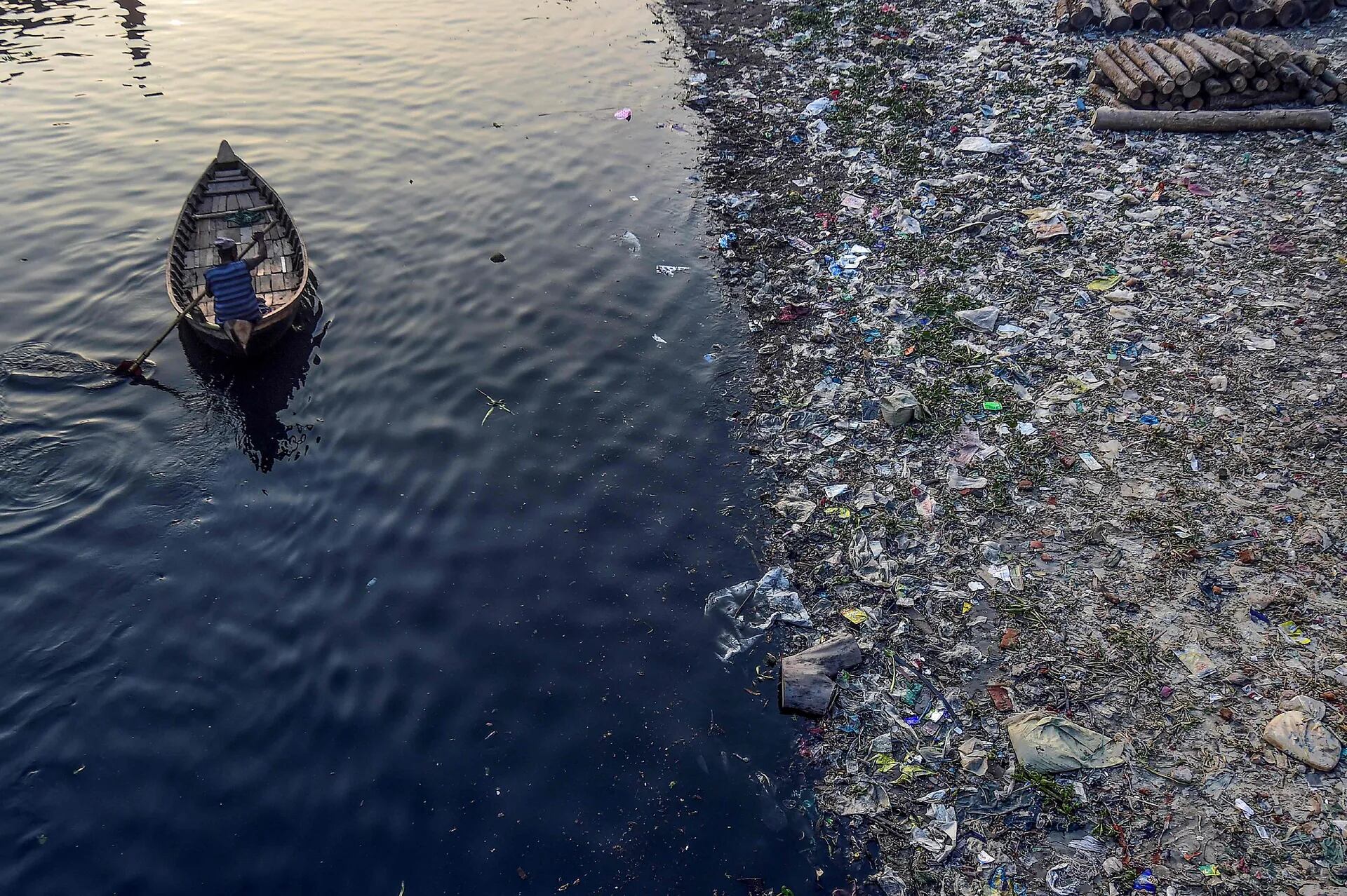 Un hombre rema en un bote mientras bolsas de plástico flotan en la superficie del agua del río Buriganga en Dhaka.