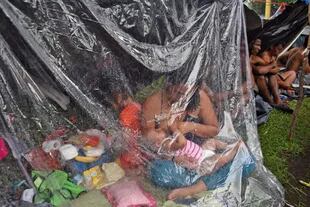 Una mujer amamanta a su bebé bajo un plástico para protegerse de la lluvia