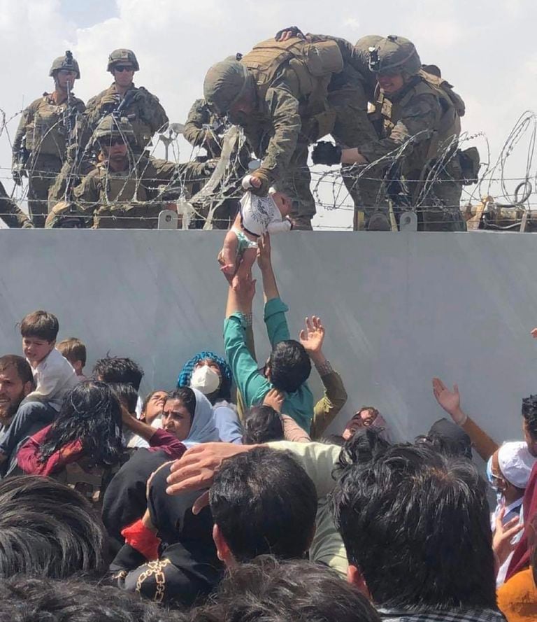 Un marine norteamericano sostiene ayer un bebé que le alcanzan los padres en el aeropuerto de Kabul