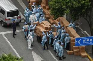 Shanghai.- Trabajadores que usan equipo de protección apilan cajas con comida sobre un carrito para entregar en un vecindario durante la cuarentena.