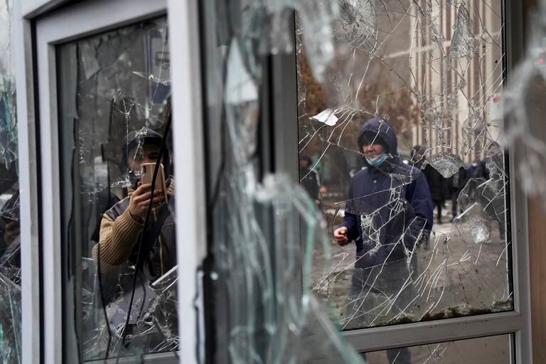 Un hombre toma una fotografía de un vidrio roto en un puesto policial vandalizado durante una protesta en Almaty, Kazajistán, el 5 de enero de 2022.  (AP Foto/Vladimir Tretyakov)