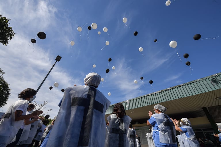 Los profesionales de la salud sostienen globos antes de liberarlos mientras honran a los colegas que murieron por el nuevo coronavirus, en las afueras del Hospital de la Universidad de Sao Paulo en Brasil, el 12 de mayo de 2020