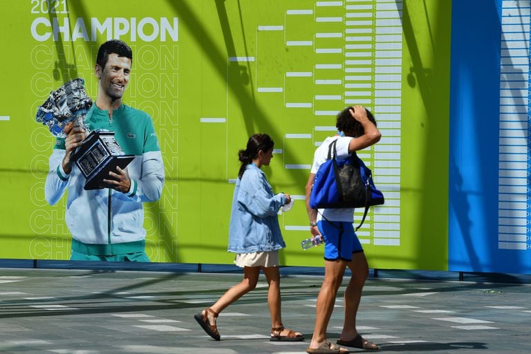 People walk past an image of Serbian tennis player Novak Djokovic on a wall at Melbourne Park in Melbourne, Wednesday, January 12, 2022. Questions are being asked about tennis world No.1 Novak Djokovic's travel documents, as his wait to learn if his visa will be cancelled continues. (AAP Image/James Ross) NO ARCHIVING