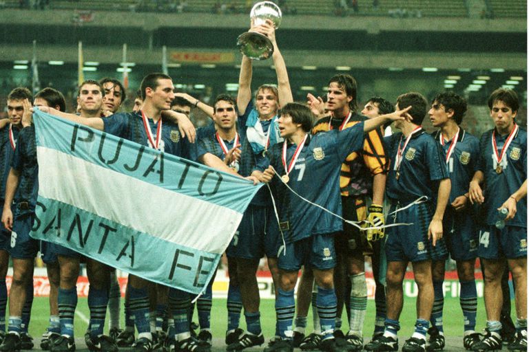 Argentina campeón en 1997, en Malasia: Scaloni posa con la bandera de Pujato, Cambiasso sostiene la copa; Placente, al final de la fila