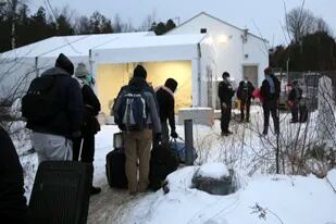 Migrantes hacen una fila en la frontera entre Estados Unidos y Canadá, en un centro de recepción para personas que cruzan a territorio canadiense sin autoridad legal, en Saint-Bernard-de-Lacolle, Quebec, Canadá, el miércoles 12 de enero de 2022, en una fotografía tomada desde Champlain, Nueva York. (AP Foto/Wilson Ring)