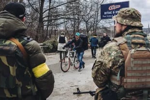 Un joven camina, junto a su bicicleta, mientras dos soldados ucranianos la observan en Irpin