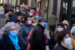 Personas usan mascarillas para frenar la propagación de COVID-19 mientras hacen fila para comprar boletos de lotería de Navidad en Madrid, España, el jueves 2 de diciembre de 2021. (AP Foto/Paul White)