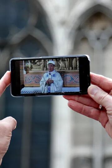 Un hombre sostiene un celular que muestra al arzobispo de París, Michel Aupetit, mientras celebra la primera misa de Notre Dame