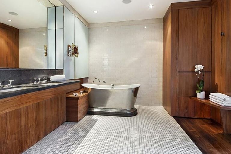 El baño cuenta con dos lavatorios, una bañadera y decoración en tonos de madera oscura y azulejos claros